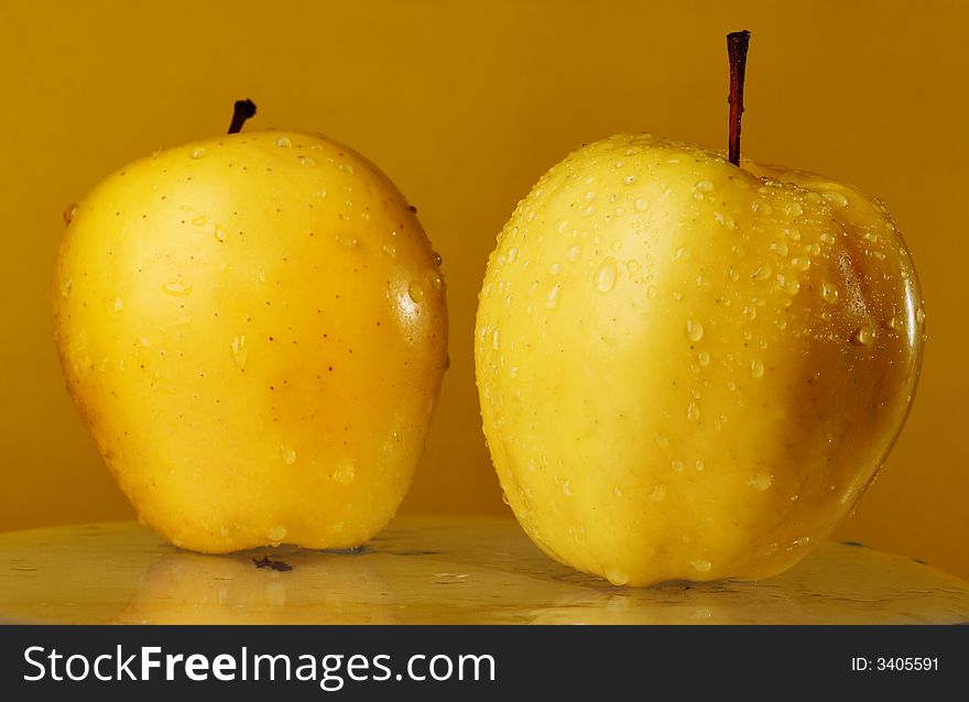 Two yellow apples on the glass over yellow background