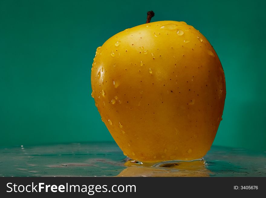 Yellow apple on the glass over green background