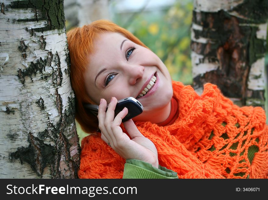 Young red-haired woman in red scarf is talking in mobile-phone. Young red-haired woman in red scarf is talking in mobile-phone