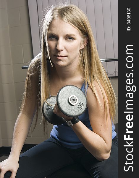 Beautiful young blond woman doing arm curls with a dumbbell in a fitness location. Beautiful young blond woman doing arm curls with a dumbbell in a fitness location.