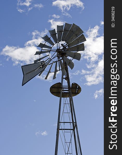 Vertical photo of antique style windmill against a blue sky with white clouds often found on small farms. Vertical photo of antique style windmill against a blue sky with white clouds often found on small farms.