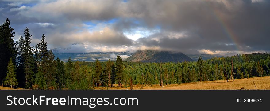 Clouds and rainbow over mountains, meadow, evergreen trees and autumn grass. Clouds and rainbow over mountains, meadow, evergreen trees and autumn grass