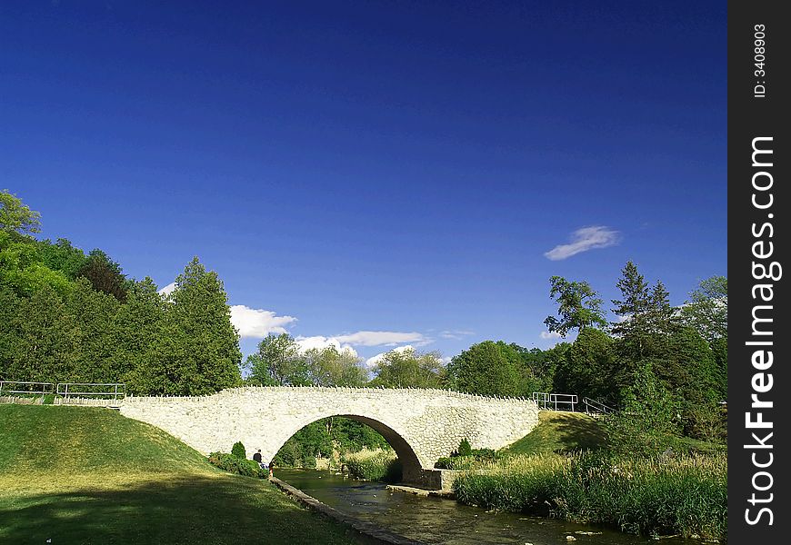 A pretty arched stone bridge over a shallow stream under a blue sky.