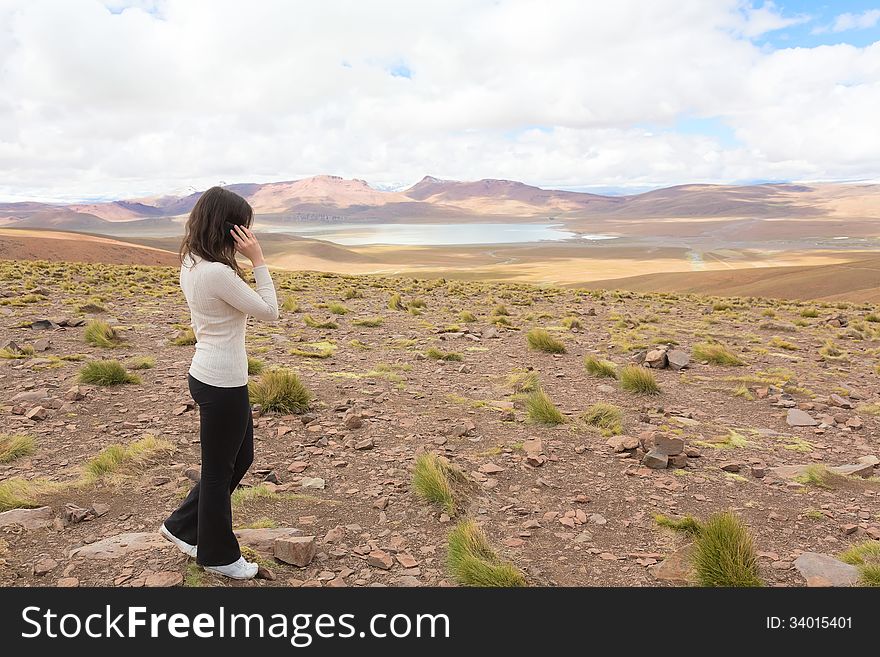 Woman talking on mobile phone and enjoing panorama of bolivian altiplano with lagoon Morejon, Bolivia
