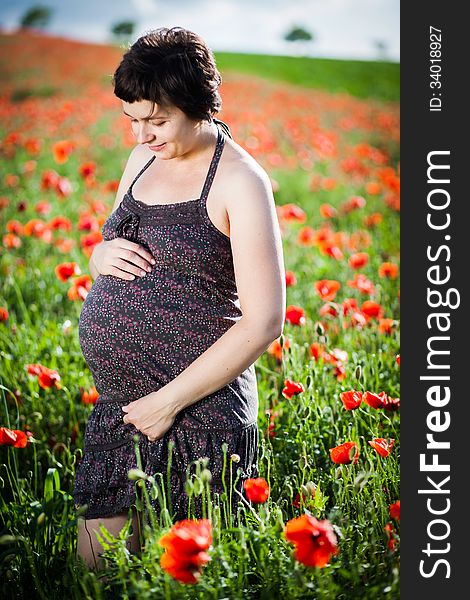 Pregnant happy woman in a flowering poppy field