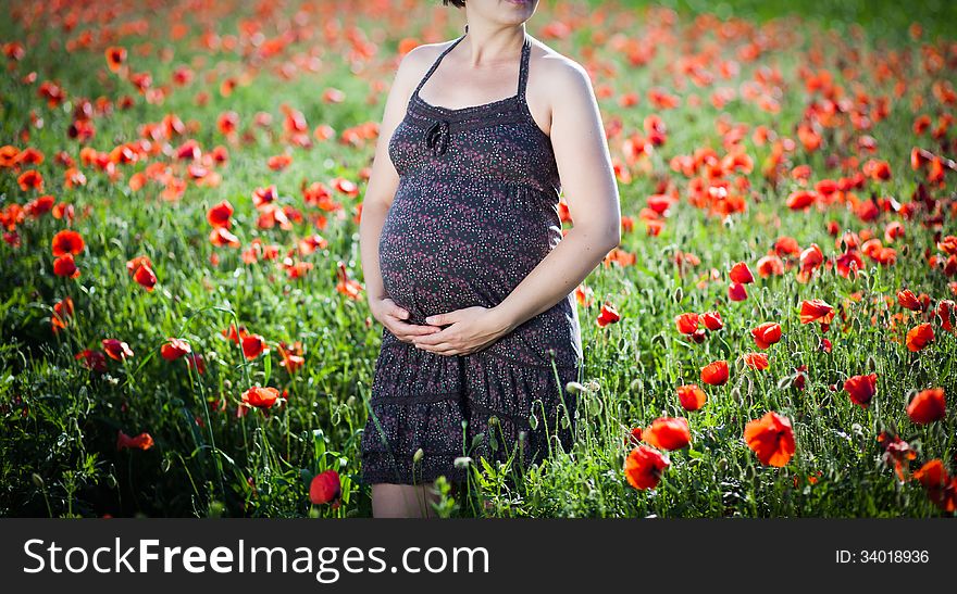 Pregnant happy woman in a flowering poppy field