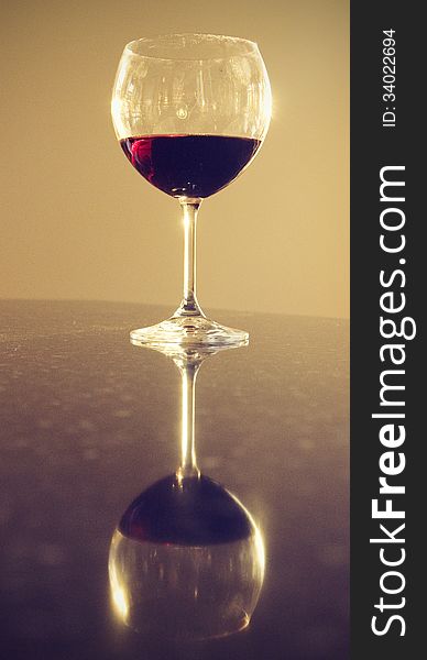 Wineglass filled with red wine sitting on granite counter showing its reflection. Wineglass filled with red wine sitting on granite counter showing its reflection.