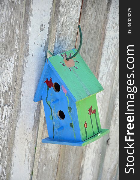 Little blue and green birdhouse hanging on wooden fence