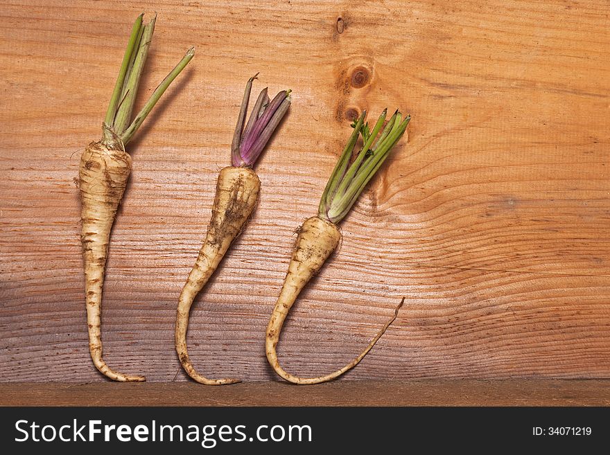 Three parsnips are arranged against a wooden board for a background and texture. Three parsnips are arranged against a wooden board for a background and texture.