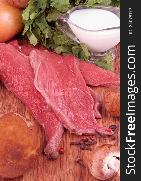 Cooking Beef Stroganoff. Arrangement of Ingredients with Raw Beef, Fresh Edible Mushrooms, Onion, Spices, Greens and Milk closeup on Wooden background