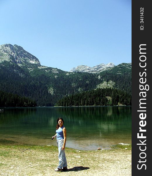 A girl in front of the glacier lake in Montenegro, caring a backpack on his shoulder, with mountains at the background. A girl in front of the glacier lake in Montenegro, caring a backpack on his shoulder, with mountains at the background