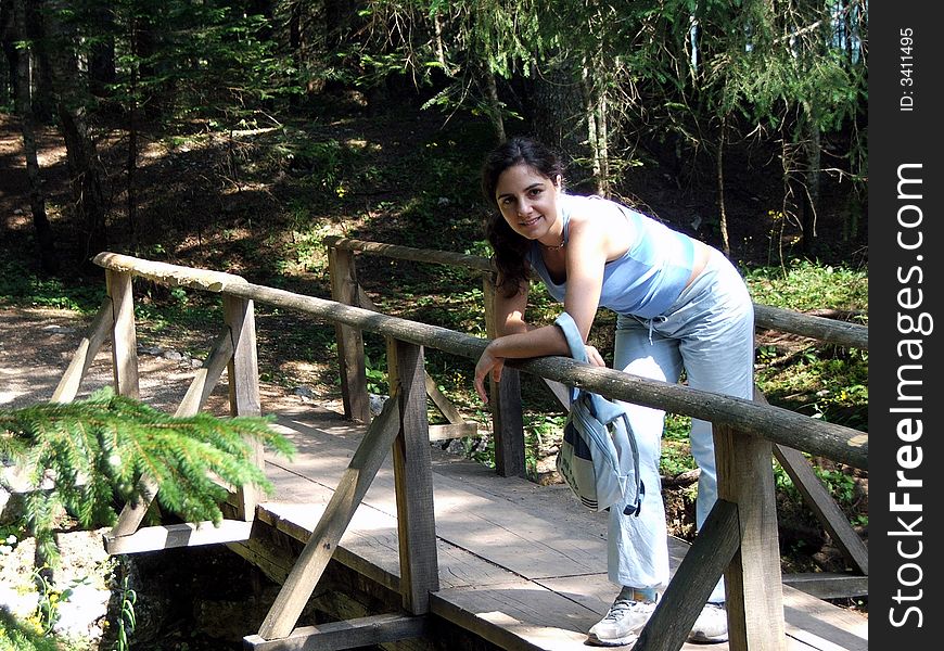 A girl, posing on a mountain bridge over a stream, resting a little bit during a walk. A girl, posing on a mountain bridge over a stream, resting a little bit during a walk