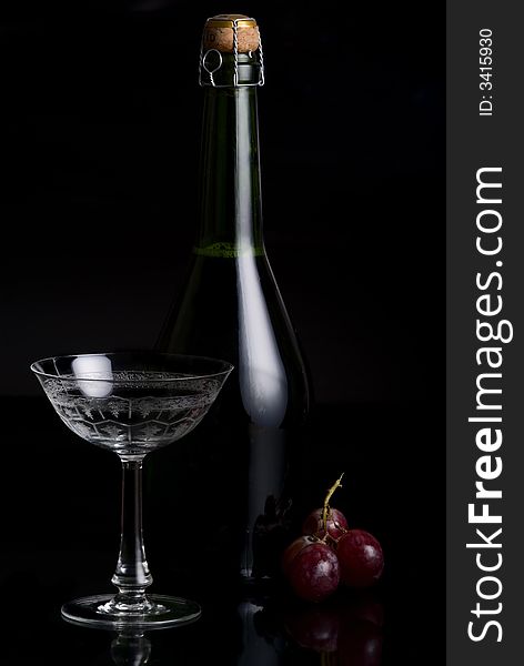 Champagne Botlte with a glass and red grape on a black background. Champagne Botlte with a glass and red grape on a black background