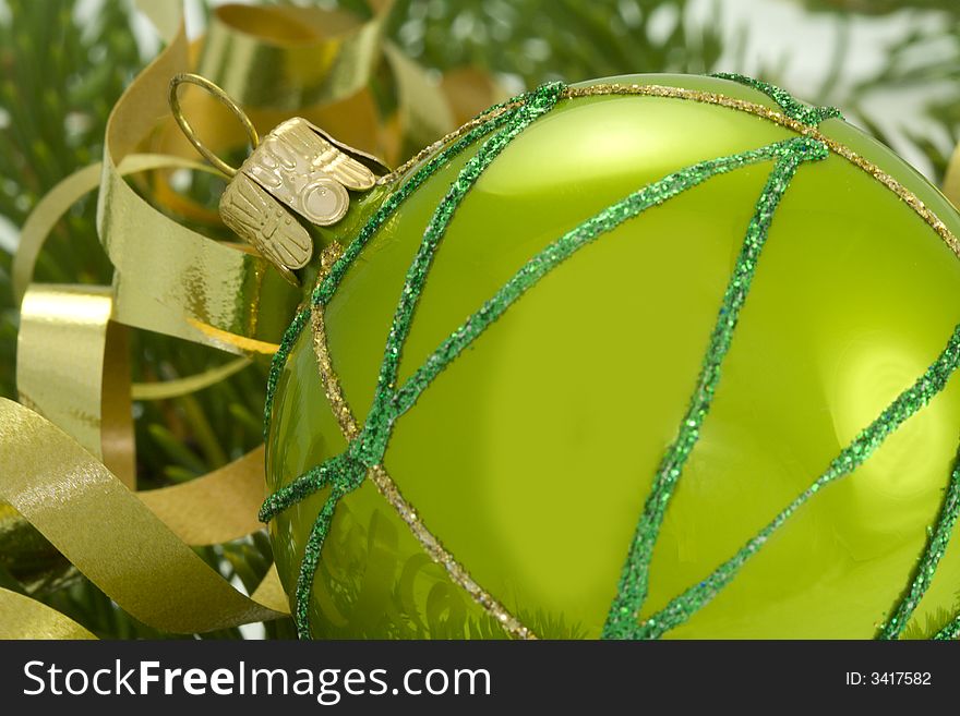 Green ornamental ball ith gold ribbon with pine branch on background