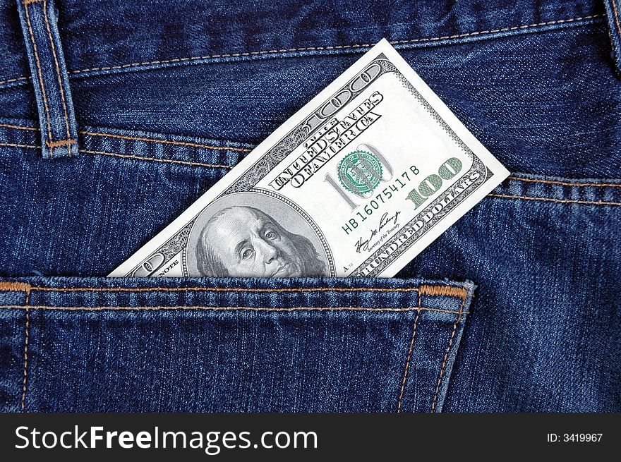 A one hundred dollar bill in the back pocket of denim trousers.  Photographed in a studio. A one hundred dollar bill in the back pocket of denim trousers.  Photographed in a studio.