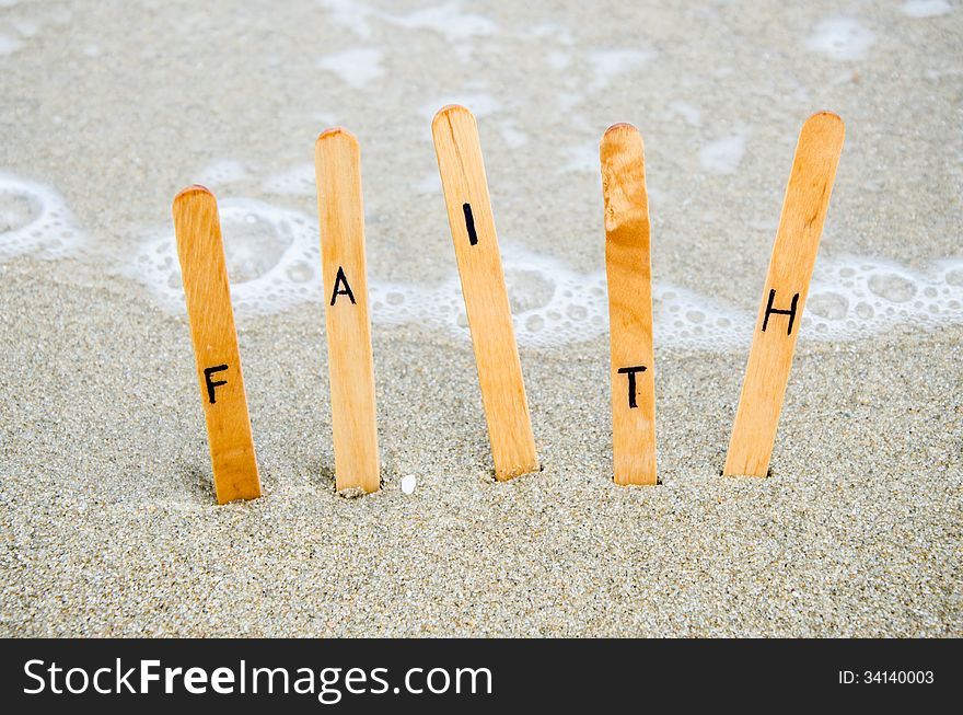 Faith text on wood pin on the sand.