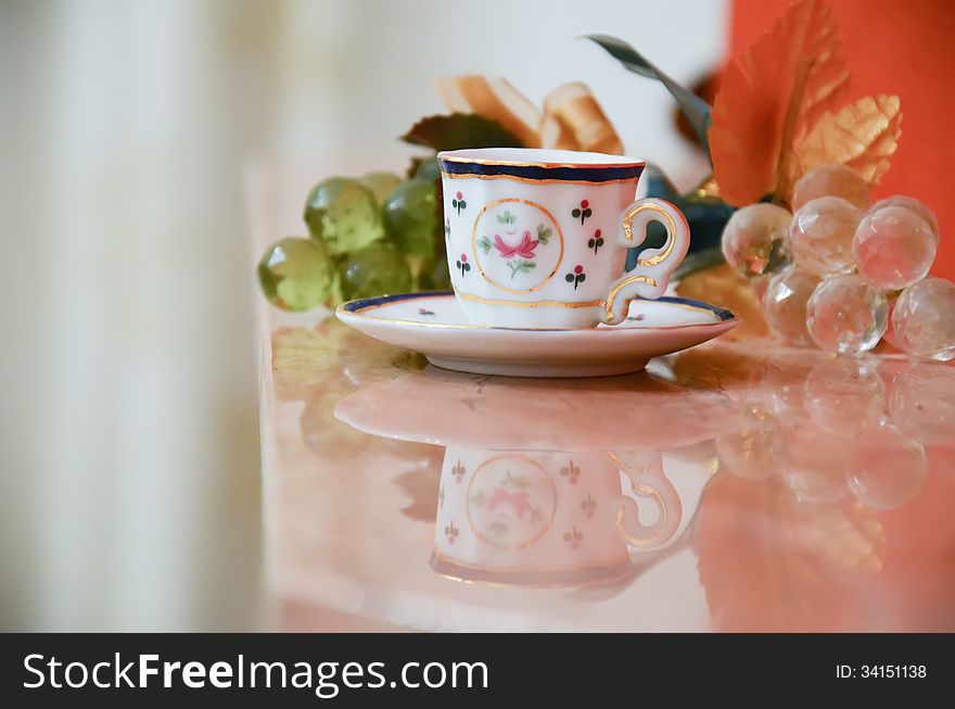 Teacup with glass grapes on a marble surface. Teacup with glass grapes on a marble surface