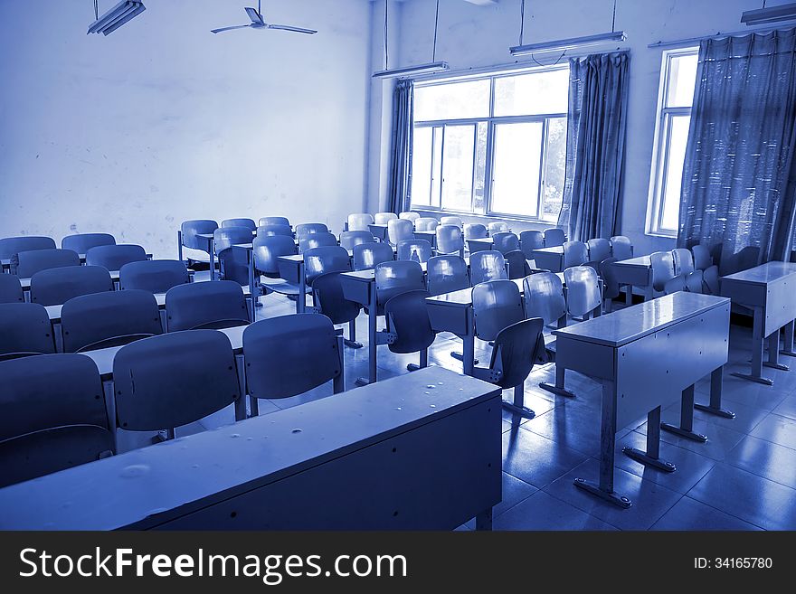 Neat rows of school desks in classroom with blue tones