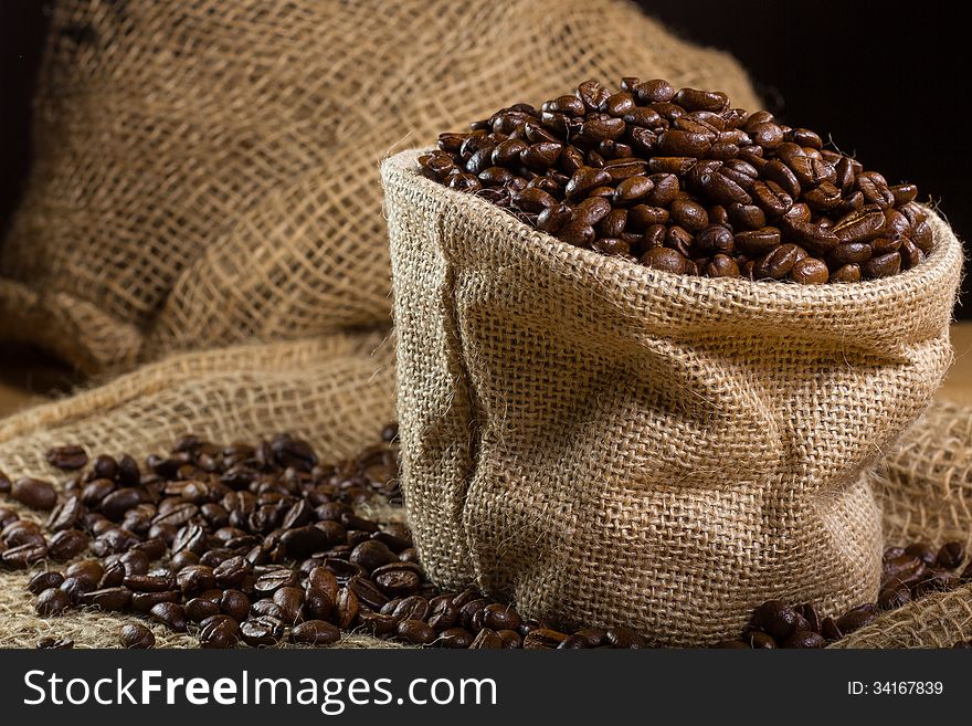 Black roasted coffee beans in a small burlap sack