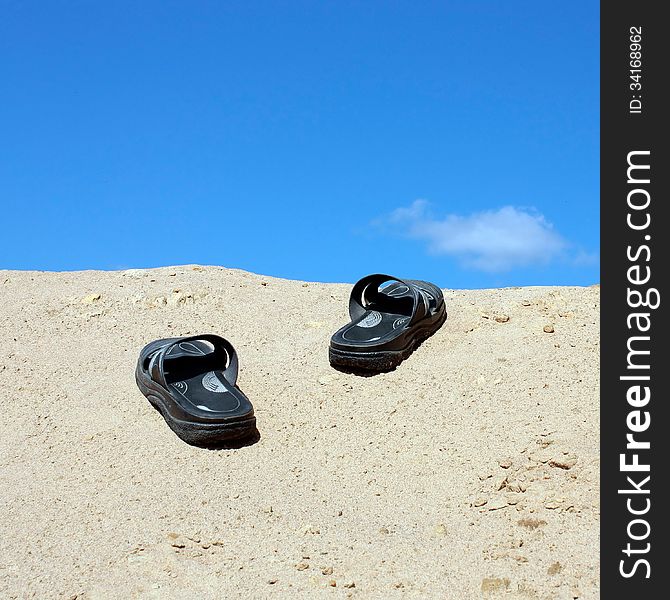 Sandals on a sandy hill on a background of bright blue sky