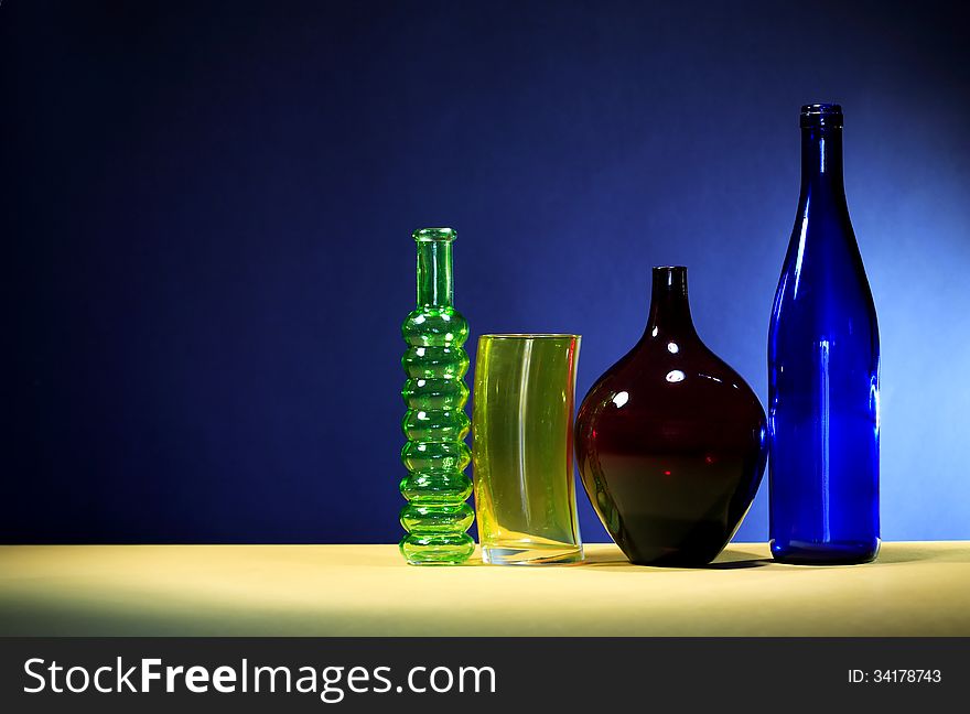 Few various colored bottles in a row against dark blue wall. Few various colored bottles in a row against dark blue wall