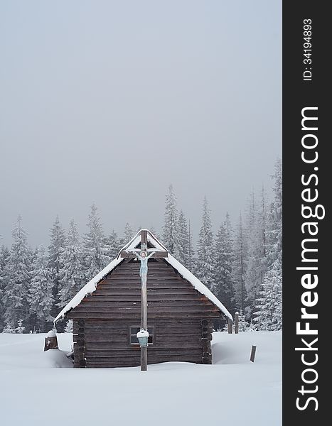Winter landscape with a wooden hut in the mountains and the Orthodox cross. Ukraine, Carpathian Mountains