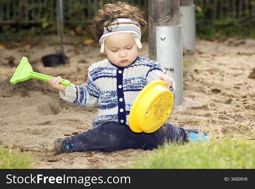 The one year old child is played in a sandbox. The one year old child is played in a sandbox.
