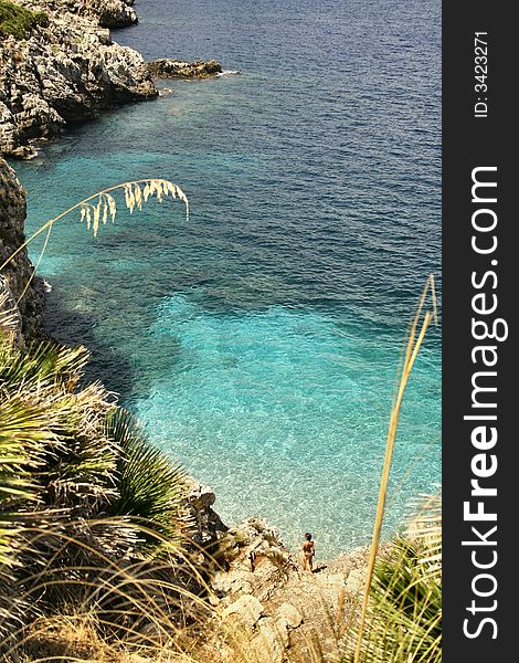 Beautiful sea pool view from above, rocks and plants all around, very transparent sea and a small child in swim suit waiting for a dip. Beautiful sea pool view from above, rocks and plants all around, very transparent sea and a small child in swim suit waiting for a dip