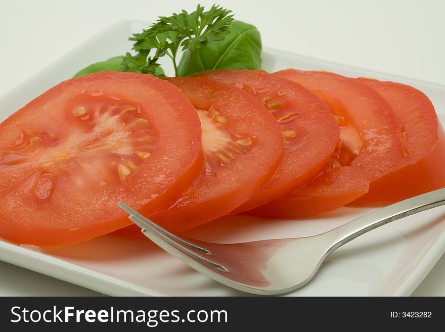 Sliced tomato on a whit plate with spoon and decorated with persil