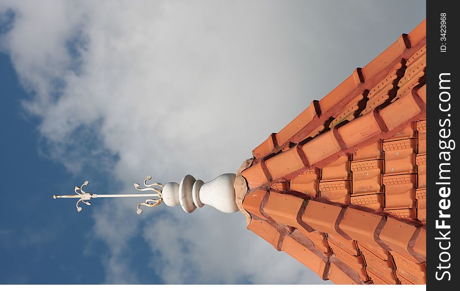 Decorative lightening rod on the top of a tiled tower roof.  Blue sky background. Decorative lightening rod on the top of a tiled tower roof.  Blue sky background