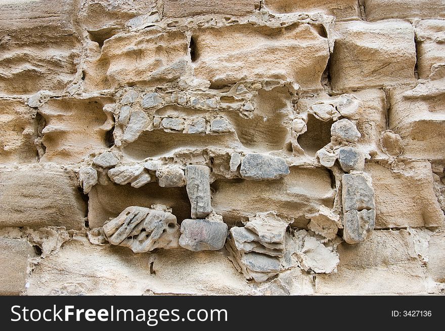 Weathered ancient stone wall, the soft stone and masonry eroded by the passage of time and the effects of rain and wind