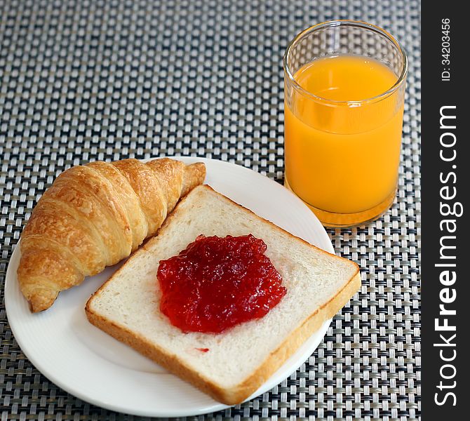 Strawberry jam on bread, croissant  and orange juice