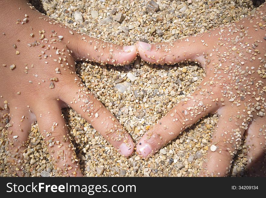 Heart symbol made by children hands on beach sand