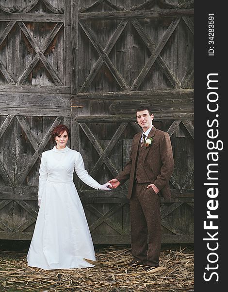 Bride and groom dressed in vintage dress and suit holding hands with wooden door behind them. Bride and groom dressed in vintage dress and suit holding hands with wooden door behind them.