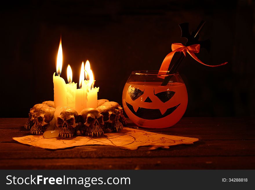 Orange Halloween drink with evil candles on wooden table in the darkness