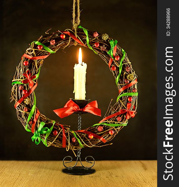 Christmas wreath with burning candle and red bow on wooden table and black background. Christmas wreath with burning candle and red bow on wooden table and black background