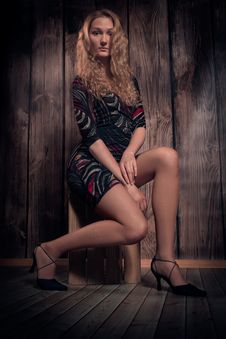 Beautiful Blond Curly Hair Model Sitting In A Pose On The Box Over Wooden Wall Background Royalty Free Stock Image