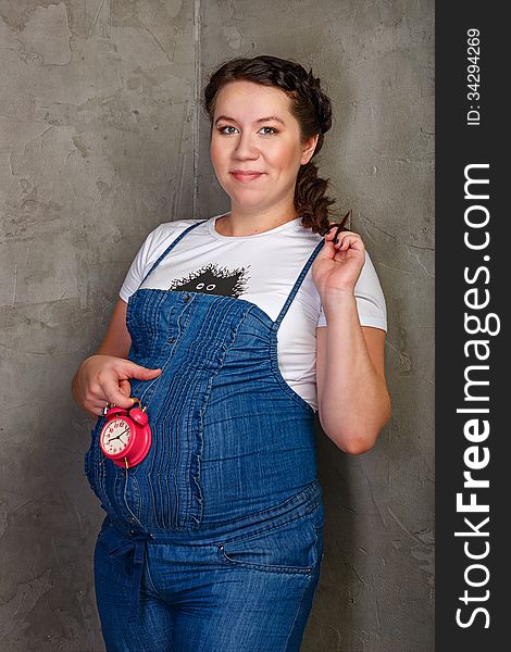 Pregnant girl in denim overalls with a clock in his hands. Pregnant girl in denim overalls with a clock in his hands