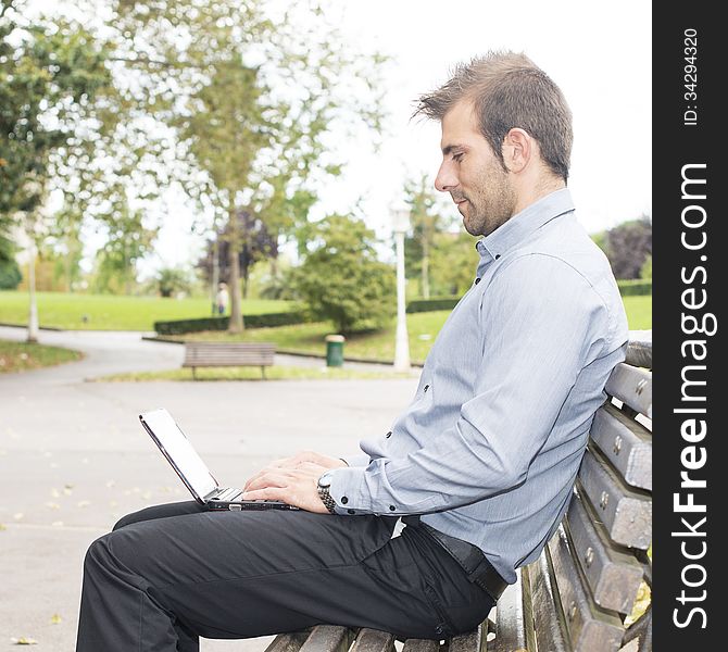 Man Sitting In The Wooden Bench And Working With Computer.