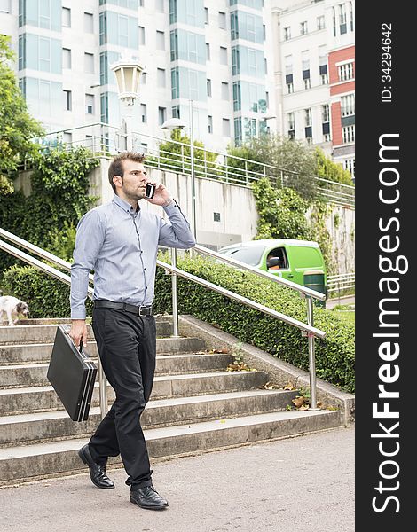 Businessman with briefcase talking by phone in the street.