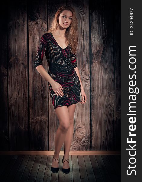 Gorgeous female model with a fine figure is wearing modern short dress and full length standing in a pose, looking straight to the camera. Wooden wall background. Gorgeous female model with a fine figure is wearing modern short dress and full length standing in a pose, looking straight to the camera. Wooden wall background.