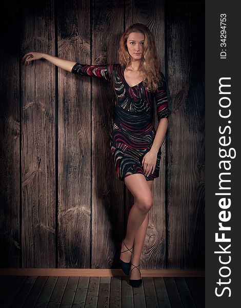 Beauty Model In Short Dress And High-heel Shoes Over Wooden Wall Background