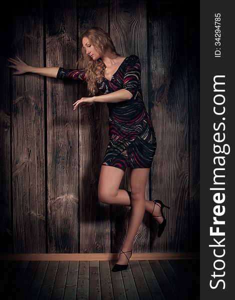 Gorgeous natural looking woman with blond long hair and fine figure is wearing modern short dress and dancing over wooden wall background. Gorgeous natural looking woman with blond long hair and fine figure is wearing modern short dress and dancing over wooden wall background.