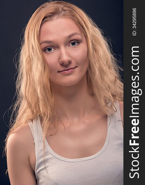Portrait of natural looking young woman with healthy facial skin, long golden blond hair, big beautiful eyes and lovely smile. Over dark blue background. Portrait of natural looking young woman with healthy facial skin, long golden blond hair, big beautiful eyes and lovely smile. Over dark blue background.