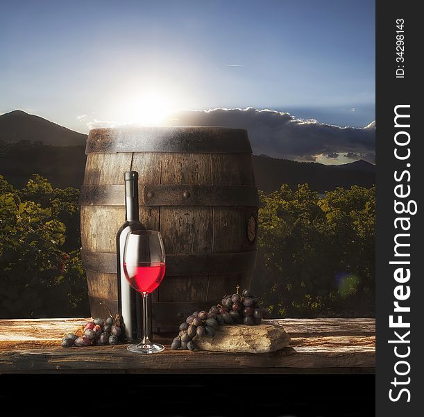 Glass red wine and bottle with old barrel on vineyard background