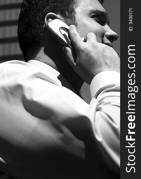 Black and white one young businessman holding cellphone to ear with building structure in background. Black and white one young businessman holding cellphone to ear with building structure in background