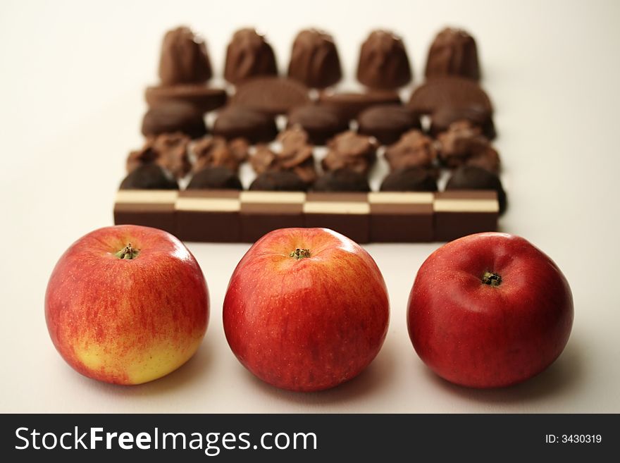 Three apples standing opposite chocolate pralines in the background. Three apples standing opposite chocolate pralines in the background.