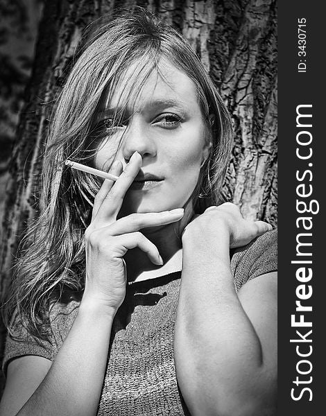 Blond smoking girl against the tree background