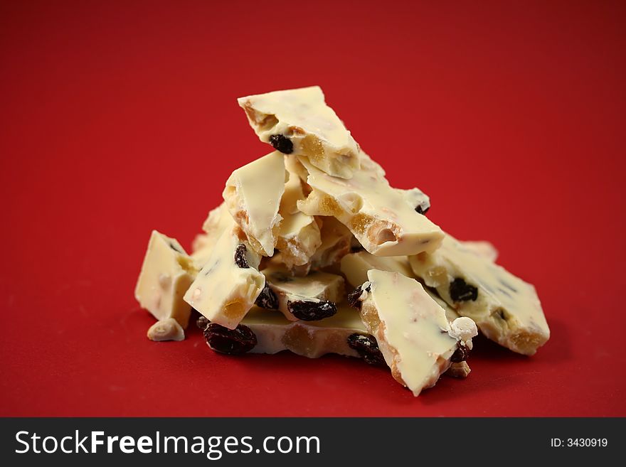 Detail of a pile of pieces of a white chocolate slab with jelly, raisins and peanuts, red background. Detail of a pile of pieces of a white chocolate slab with jelly, raisins and peanuts, red background.