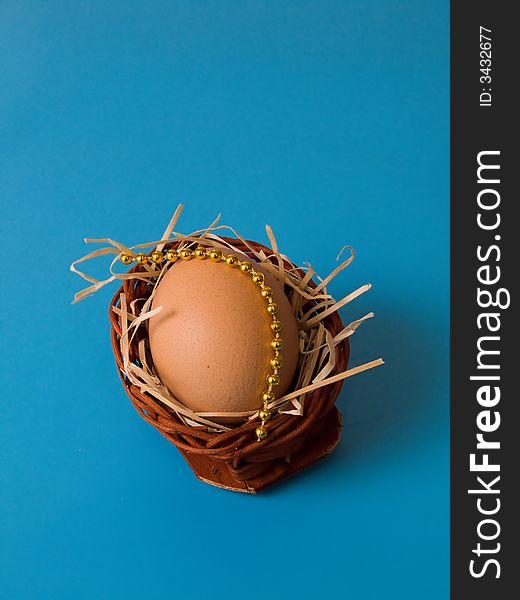 Egg in basket with beads and shavings on blue background. Egg in basket with beads and shavings on blue background
